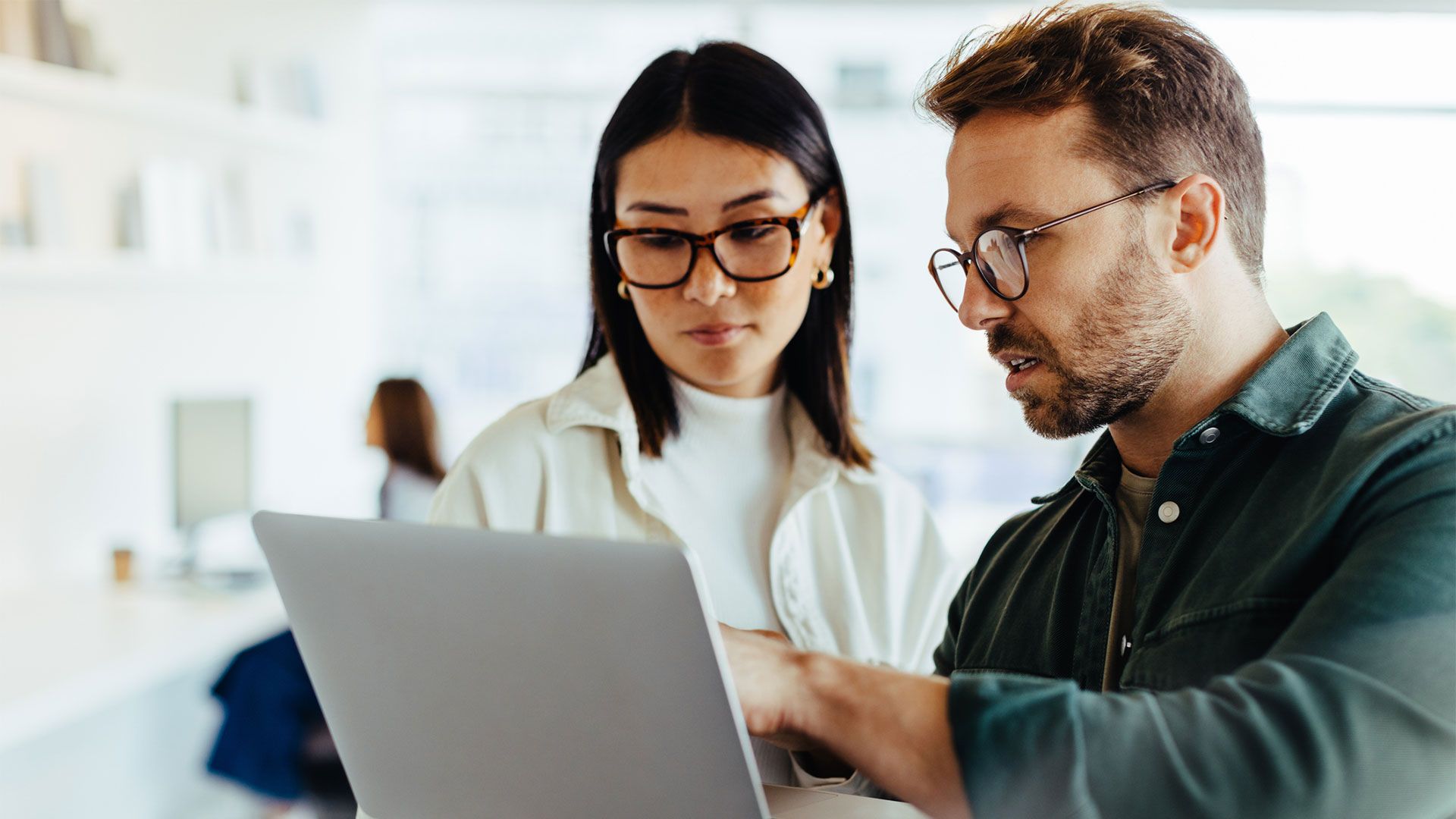 two office workers review stats in laptop