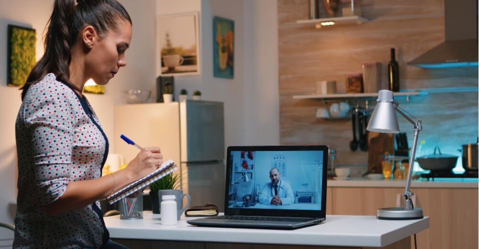 A woman sits at a desk, focused on her laptop, with a notepad and pen beside her.